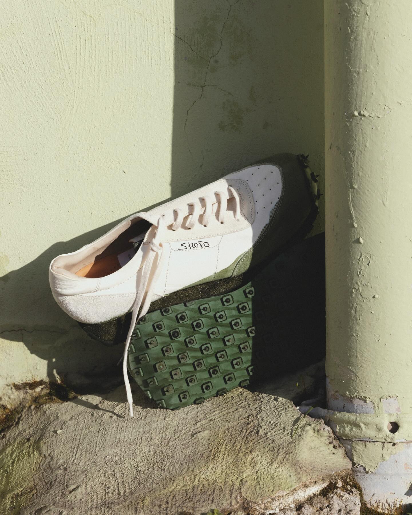 Shoto white sneaker leaning against a textured wall